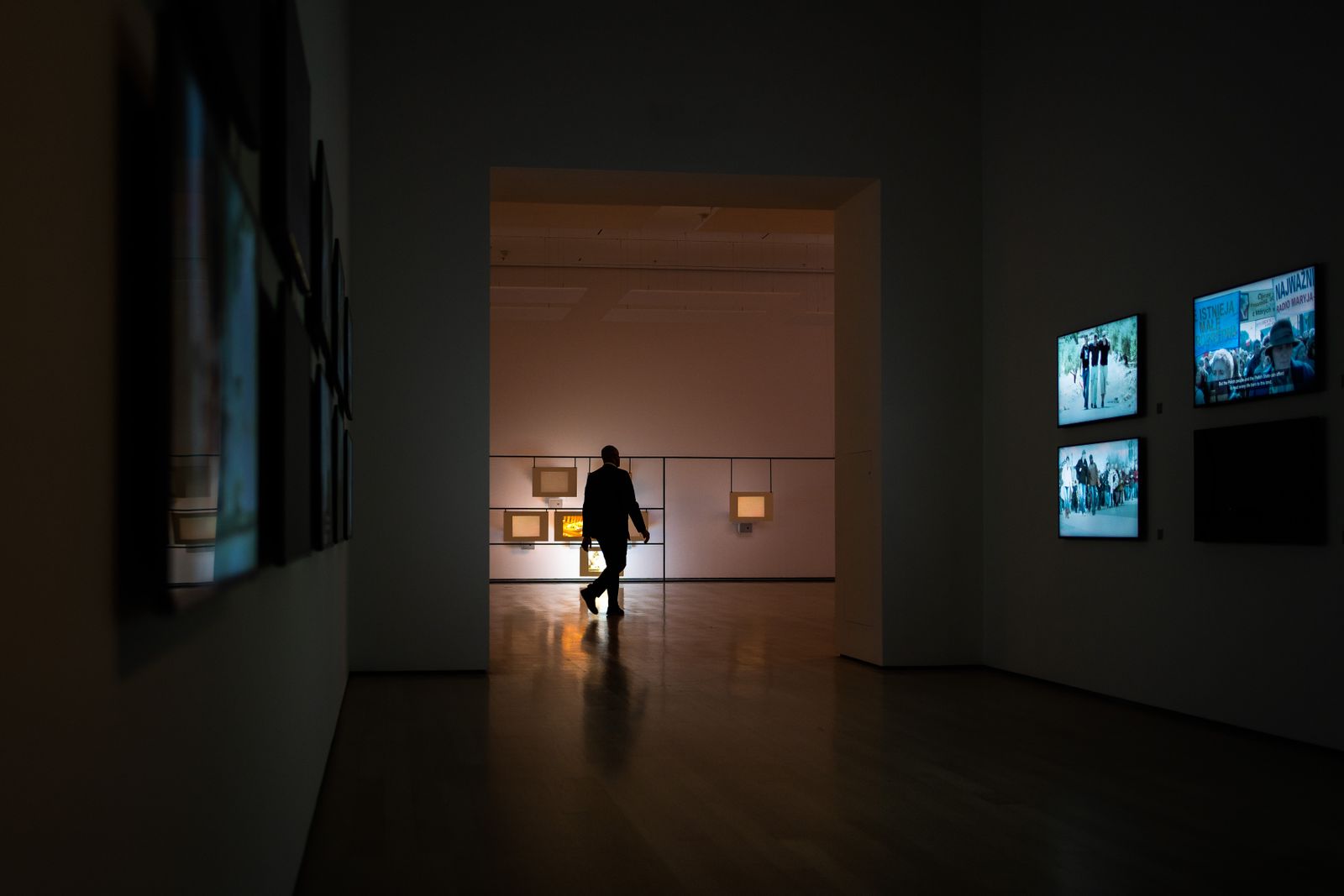 A visitor walking through a dim gallery past small glowing screens
