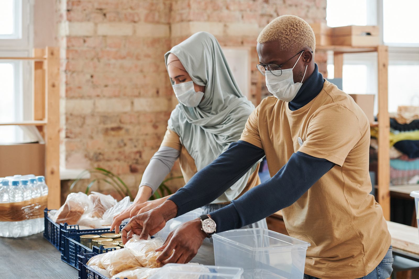 Two volunteers in gloves and masks sorting donated food into crates