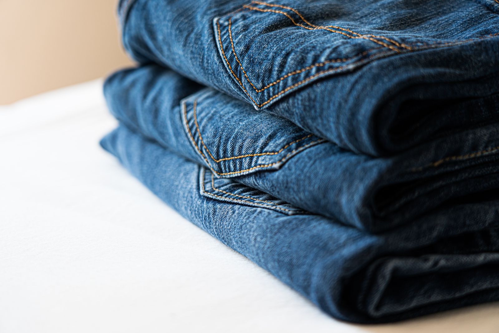 A stack of folded blue jeans on a white table, back pockets and stitching facing out