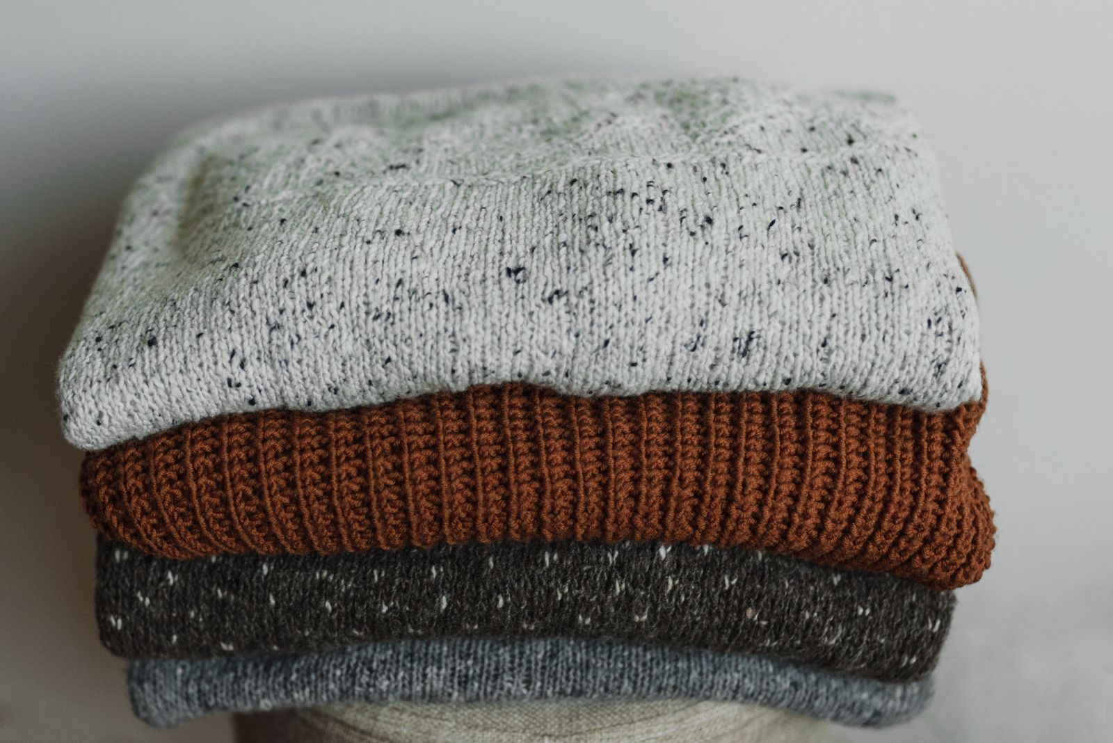 A stack of folded wool jumpers in grey, rust and charcoal