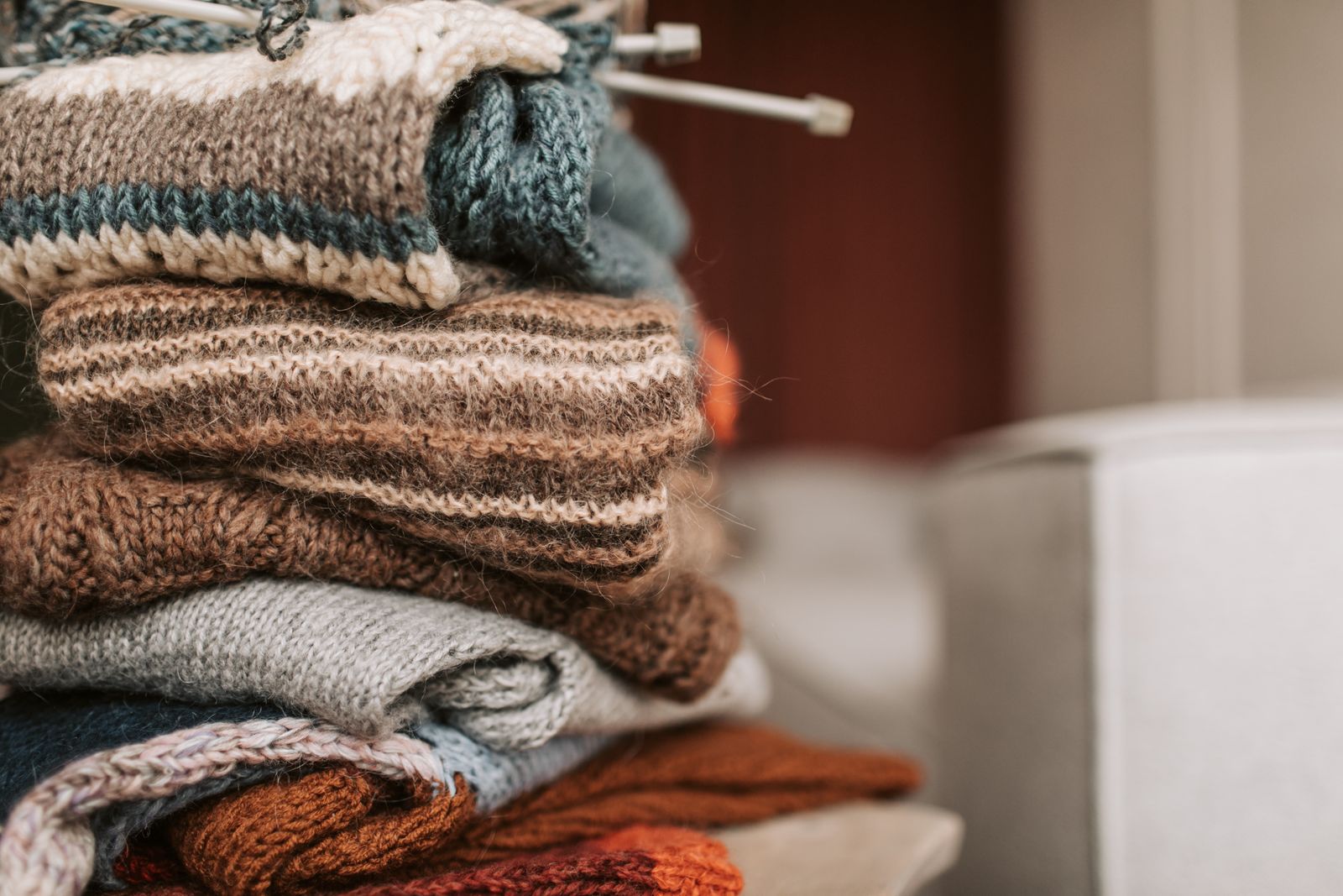 A tall stack of hand-knitted jumpers in brown, grey and rust with knitting needles on top