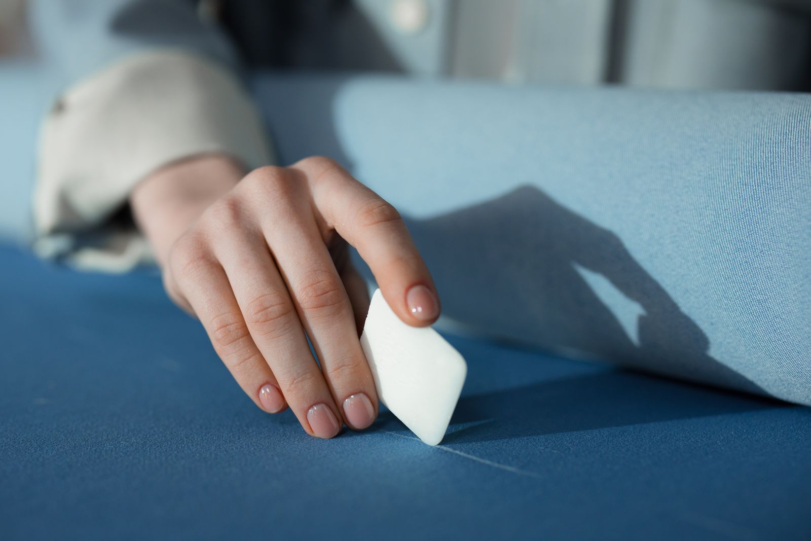 A hand drawing a line with tailor's chalk on blue cloth