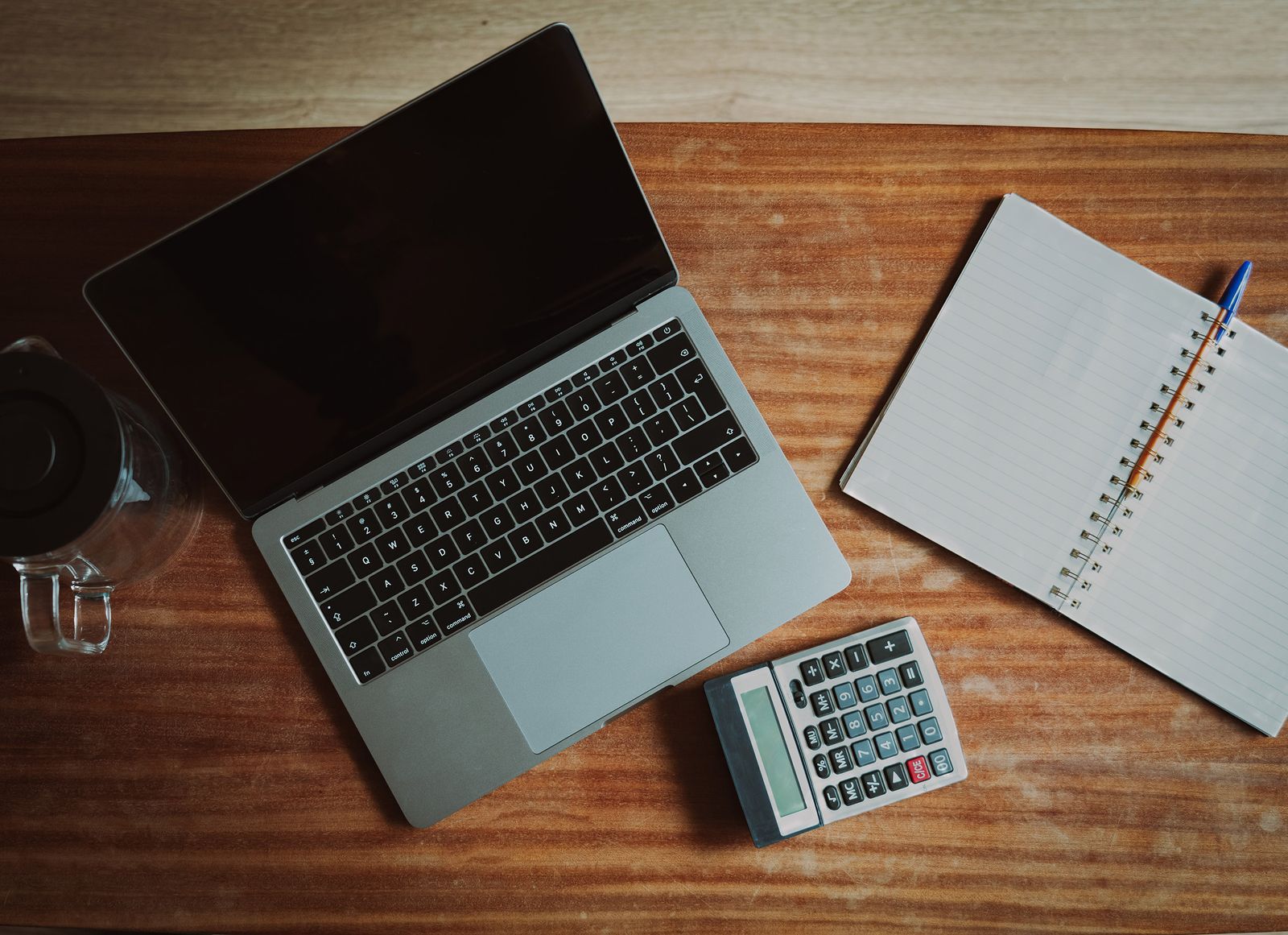 A laptop, a calculator and an open notebook on a wooden desk