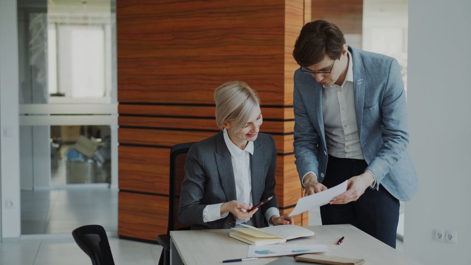Two colleagues reviewing documents at a desk by an office window
