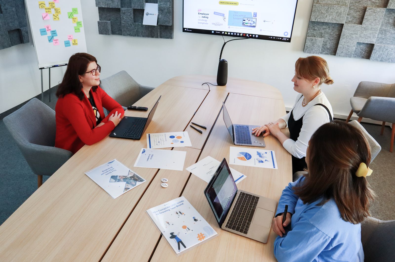 Three colleagues discussing documents and laptops at an office table