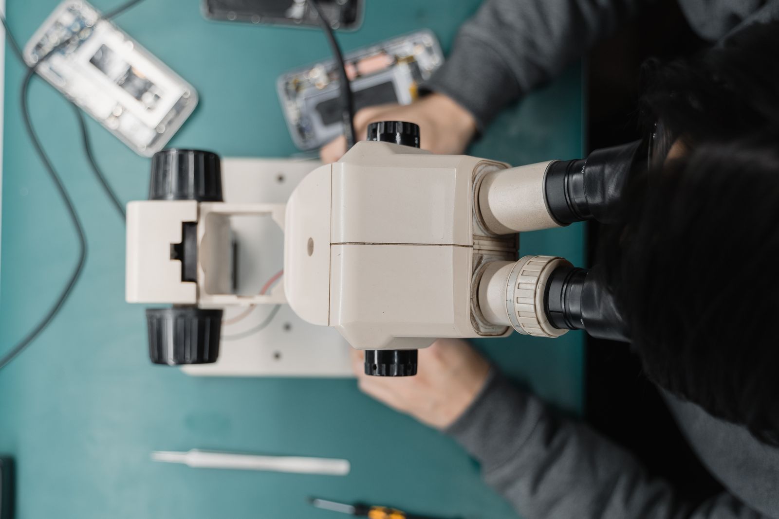 A technician working on a phone board under a stereo microscope