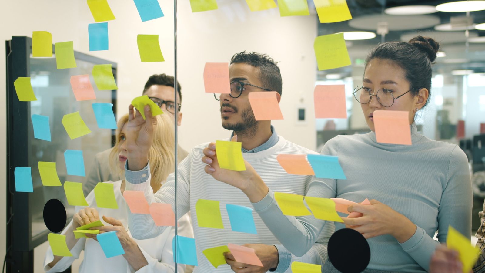 A team looking at sticky notes on a glass wall during a workshop