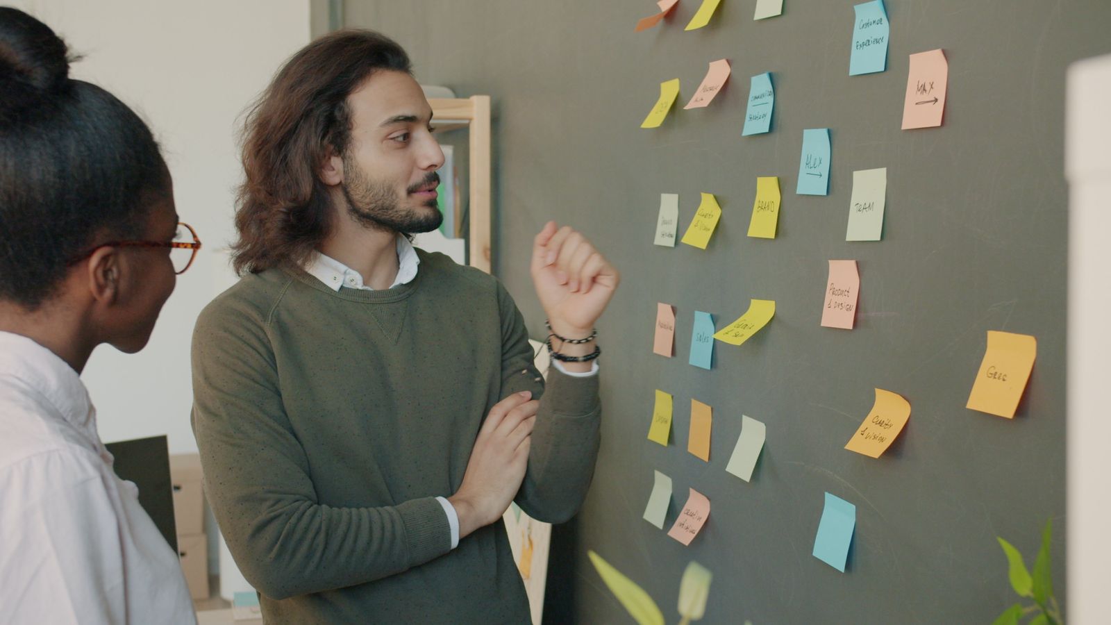 A designer explaining a wall of yellow and blue sticky notes to a colleague