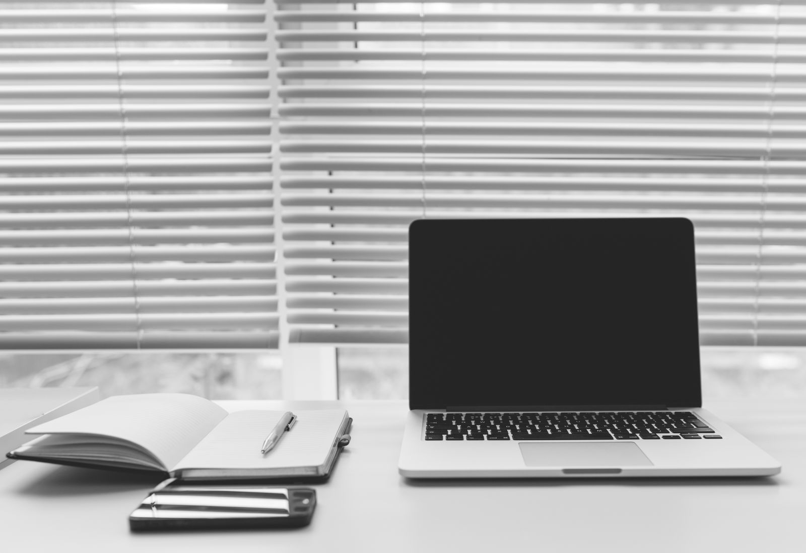 A black and white desk with a laptop, an open notebook and a phone