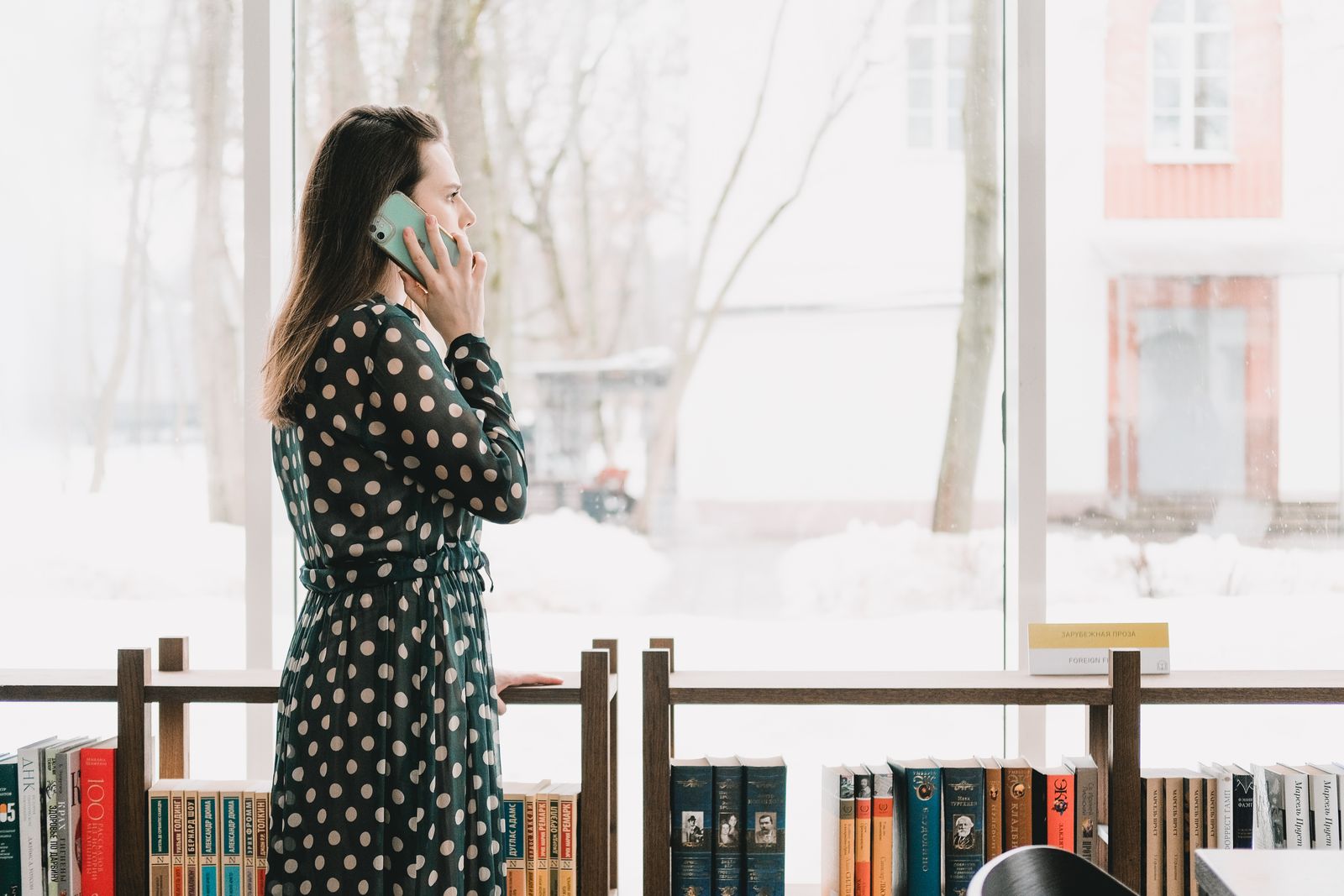 A woman talking on her phone by tall windows in a library