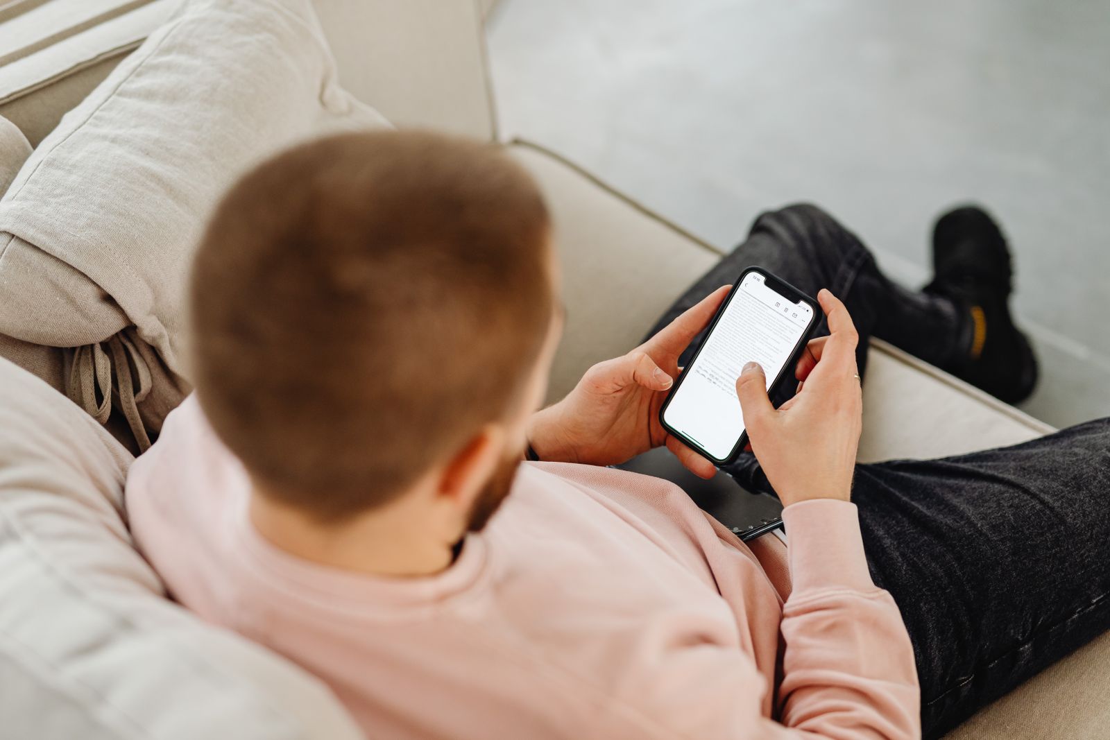 A man on a sofa reading his phone, seen from behind his shoulder