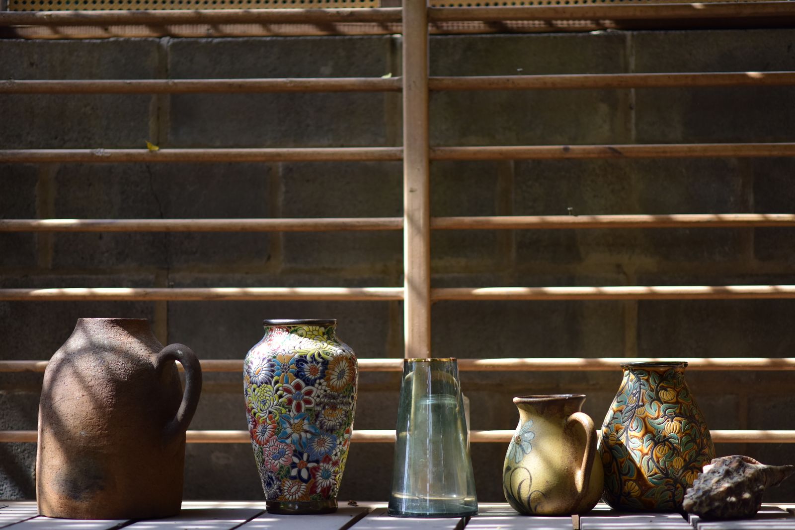 Glazed ceramic jugs and vases in brown, blue and gold on a wooden shelf in window light