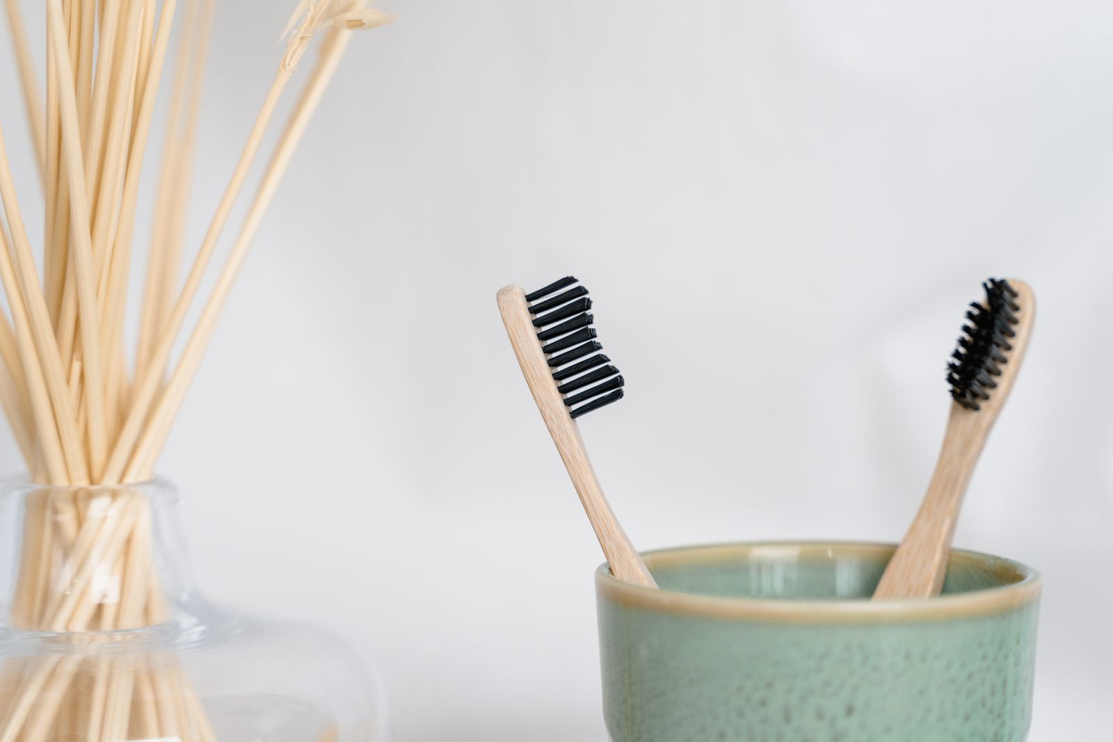 Two bamboo toothbrushes in a green ceramic cup