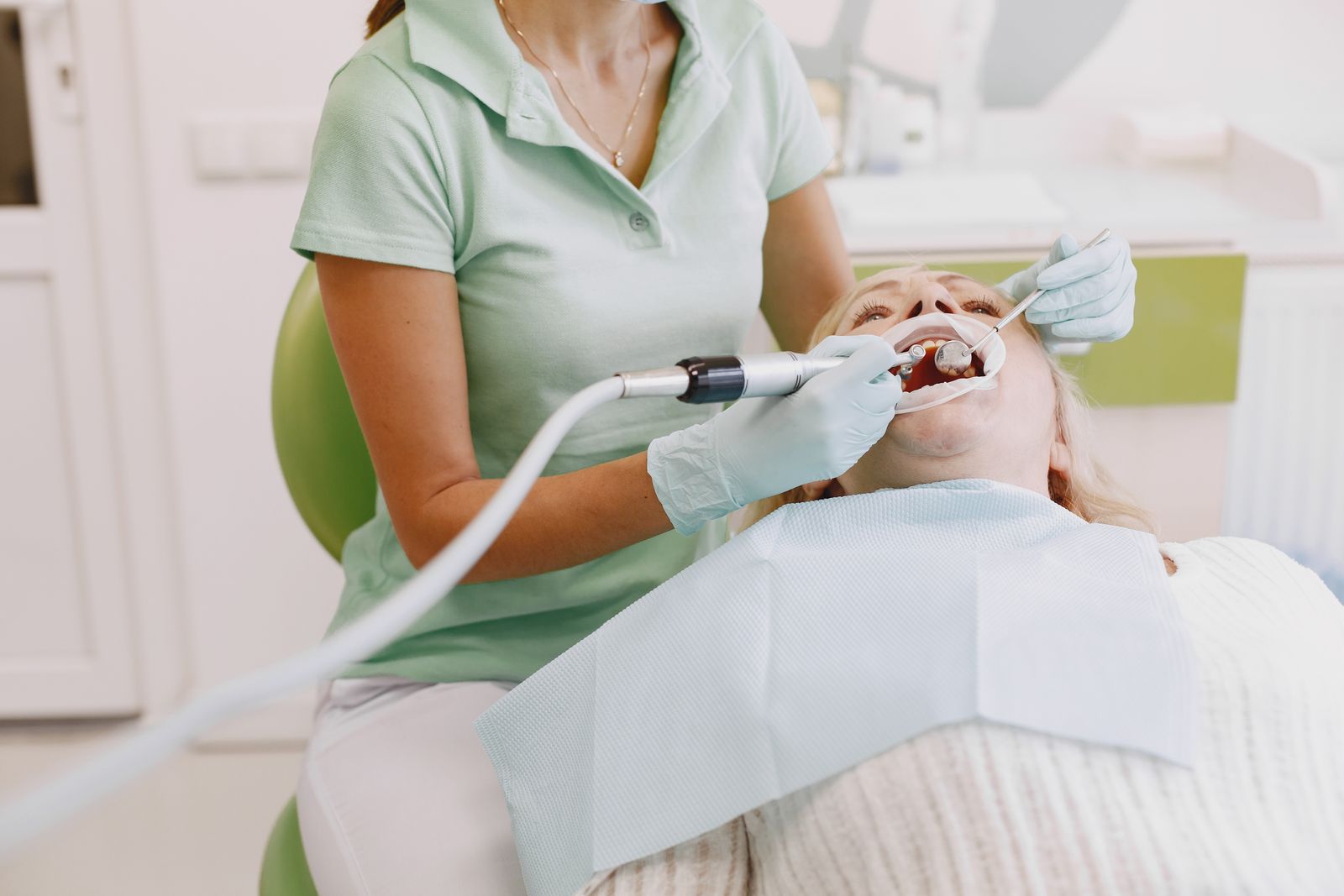 A hygienist in a mask checking a patient's teeth in the dental chair