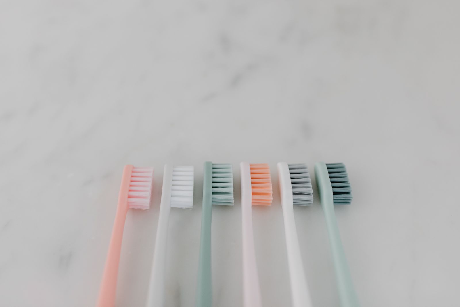 A row of pastel toothbrushes lying on a marble surface