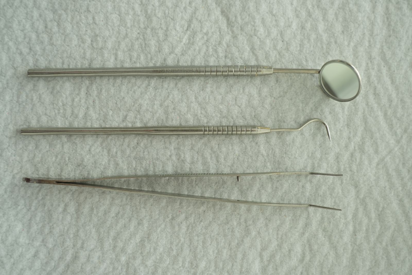 Steel dental instruments laid out in a row on a white cloth