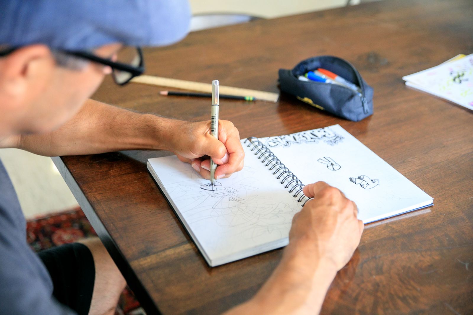 A designer drawing in a sketchbook at a wooden table