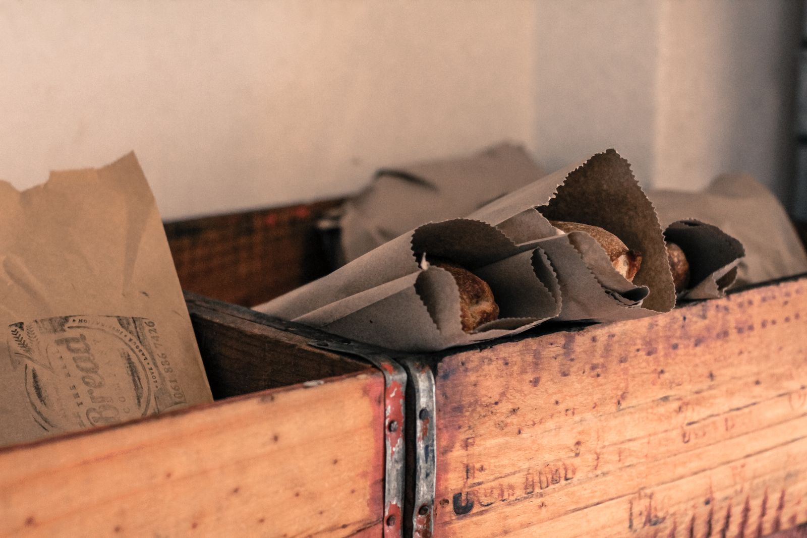 Loaves of bread wrapped in brown paper in a wooden crate