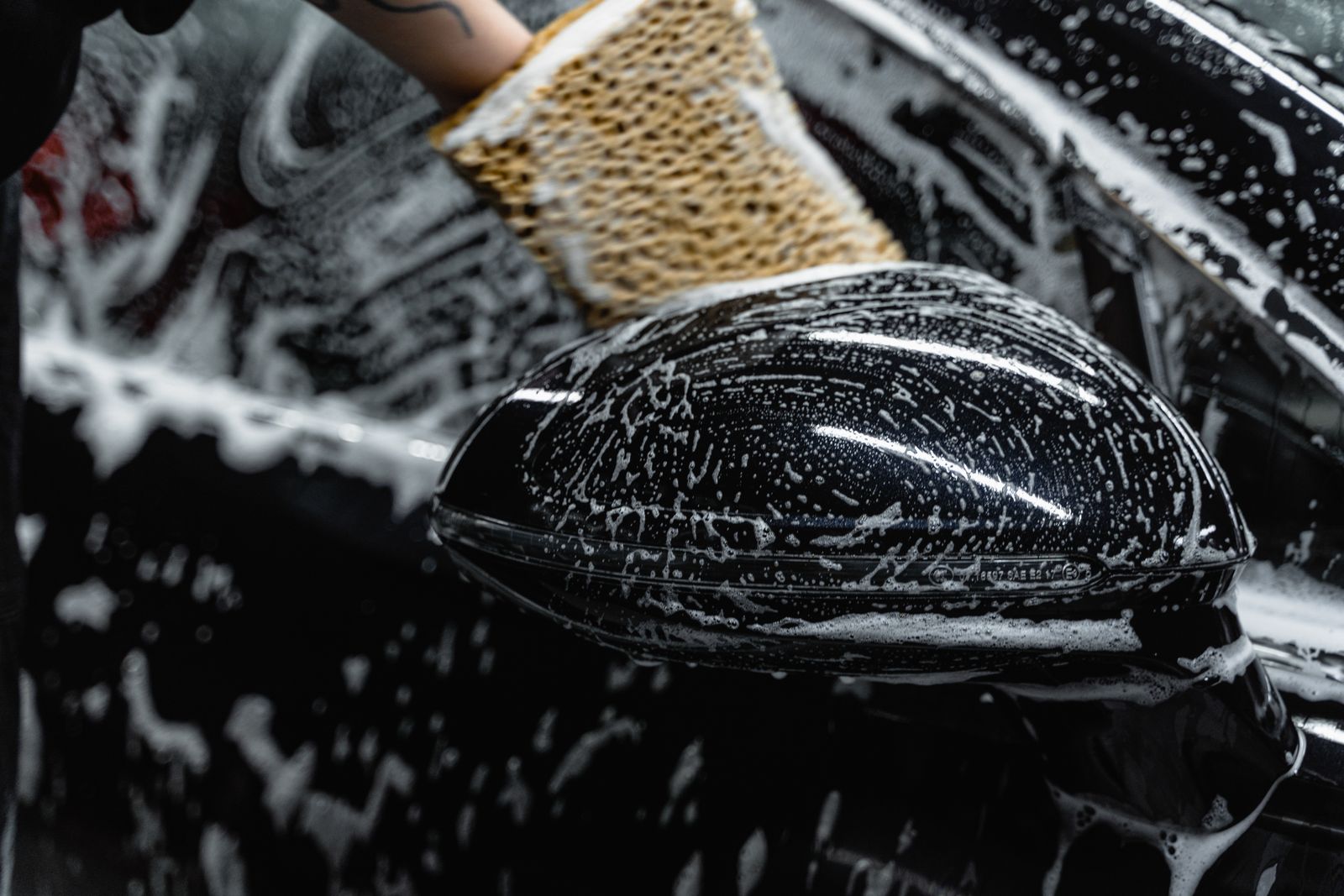 A wash mitt with foam on a black wing mirror