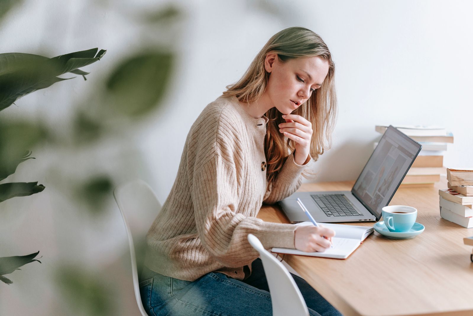 A woman writing notes in a notebook beside her laptop at home