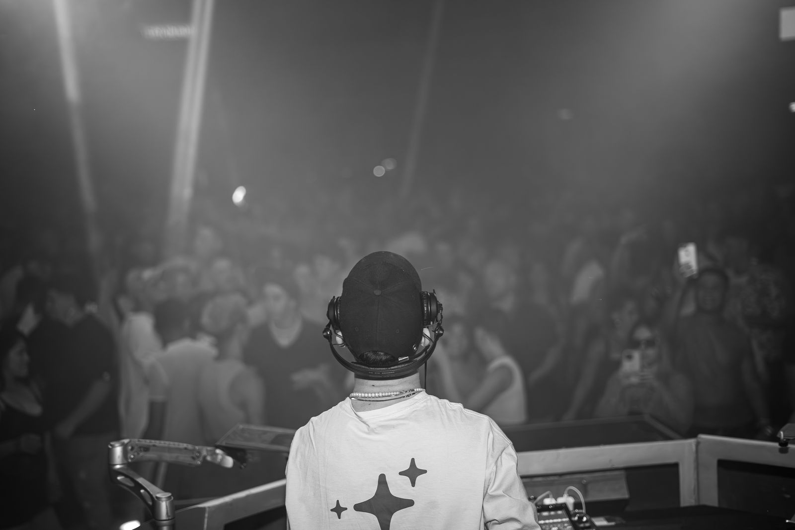 A DJ in headphones seen from behind, facing a full room