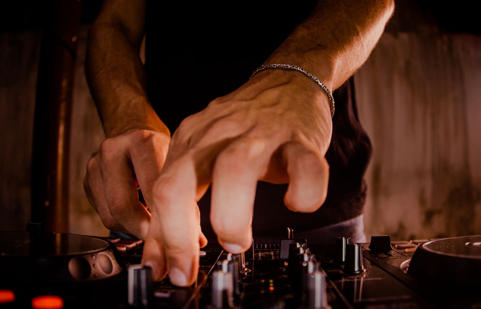 A DJ's hands turning the knobs of a mixer in warm low light