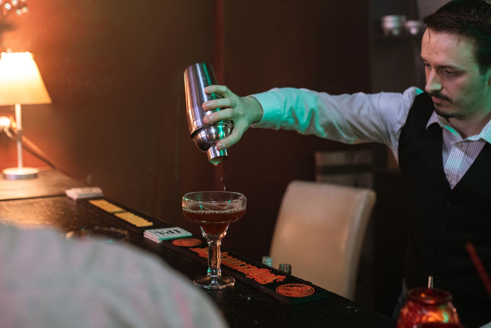 A bartender pouring a drink from a shaker into a glass