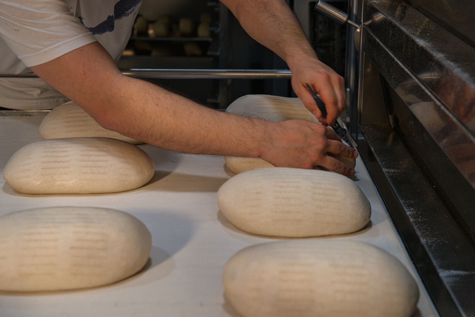 A baker shaping bread loaves on a floured tray