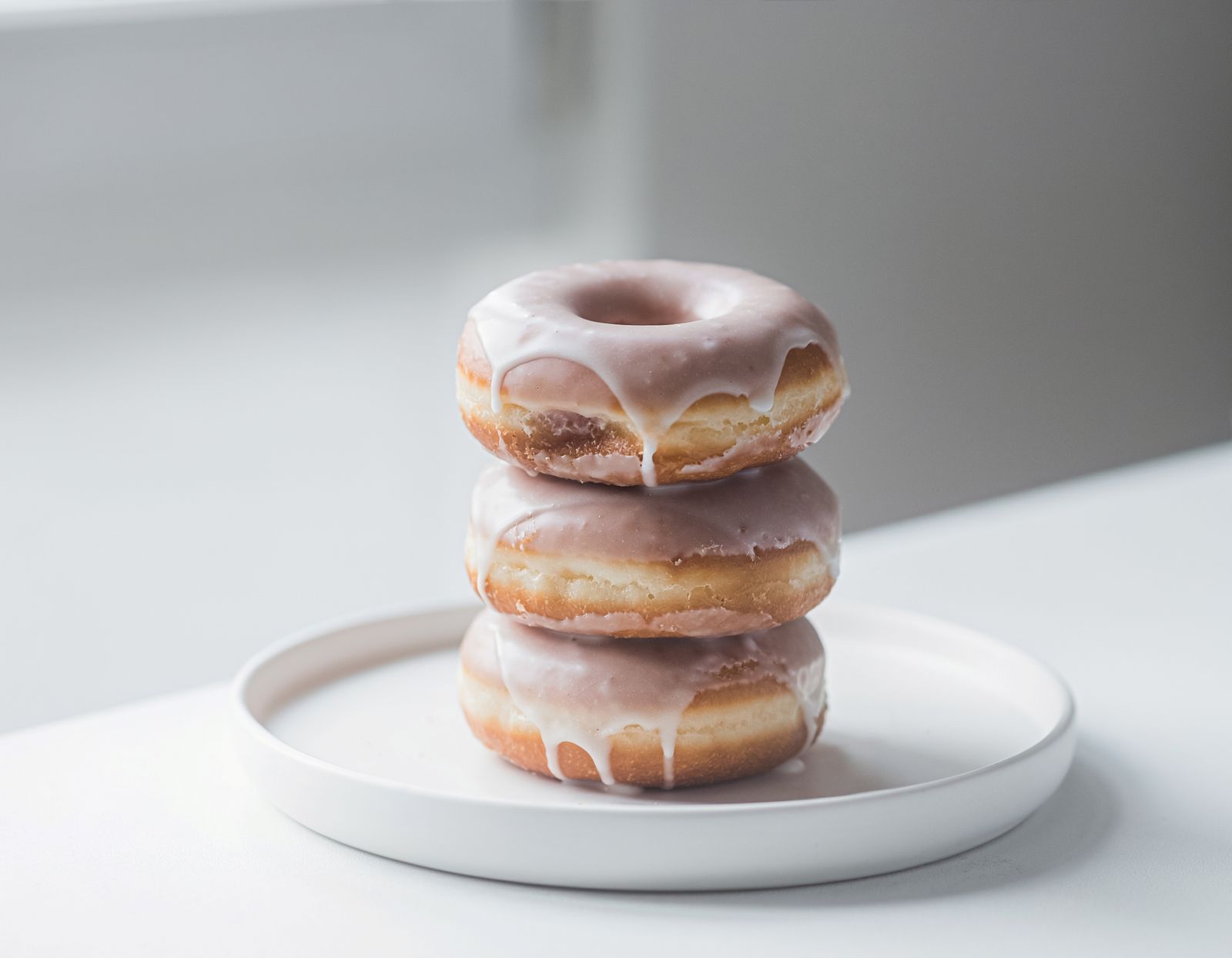 Three glazed donuts stacked on a white plate