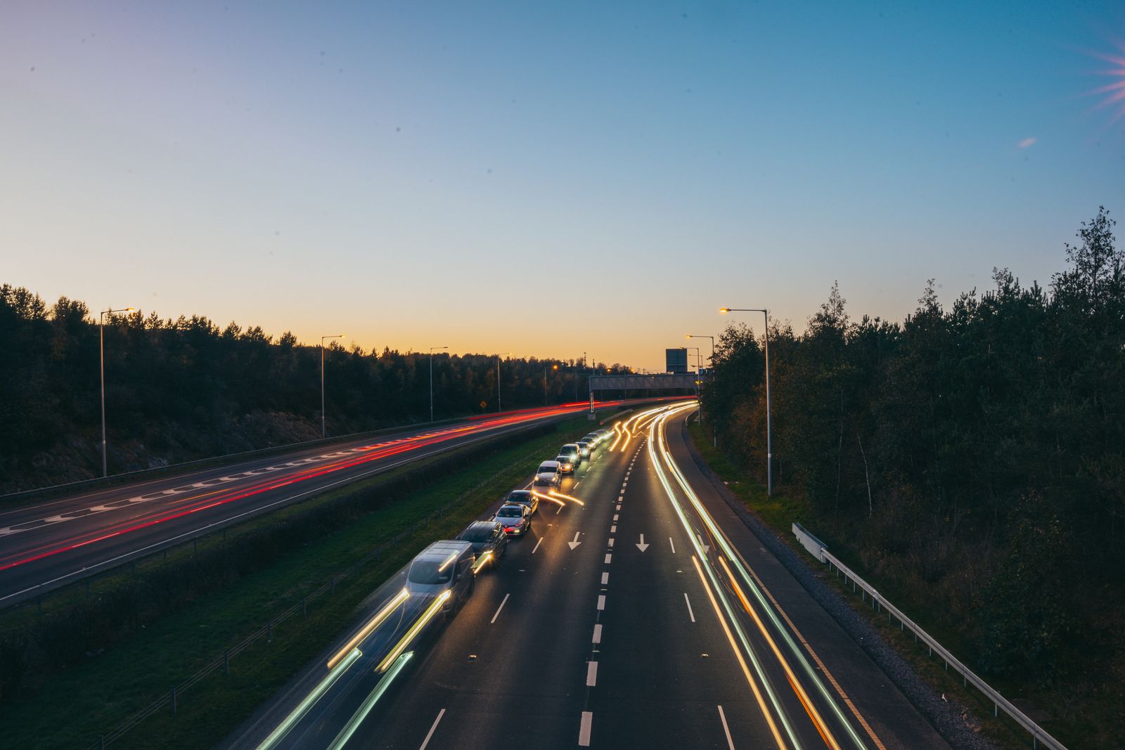 A dual carriageway at dusk with light trails from the traffic and trees on both sides