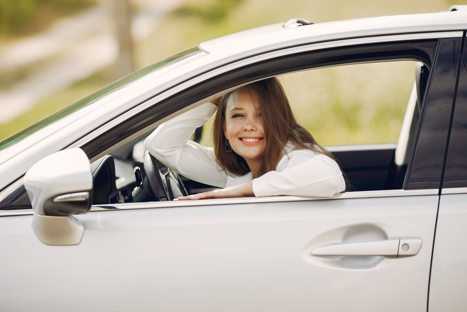 A smiling woman looking out of the open driver's window of a white car