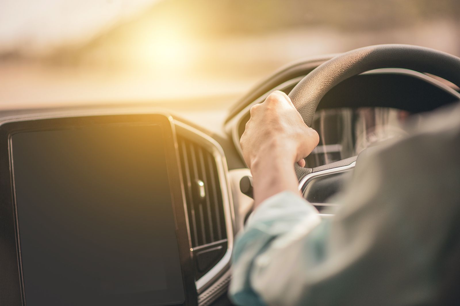 A driver's hand on the steering wheel with low sun coming through the side window