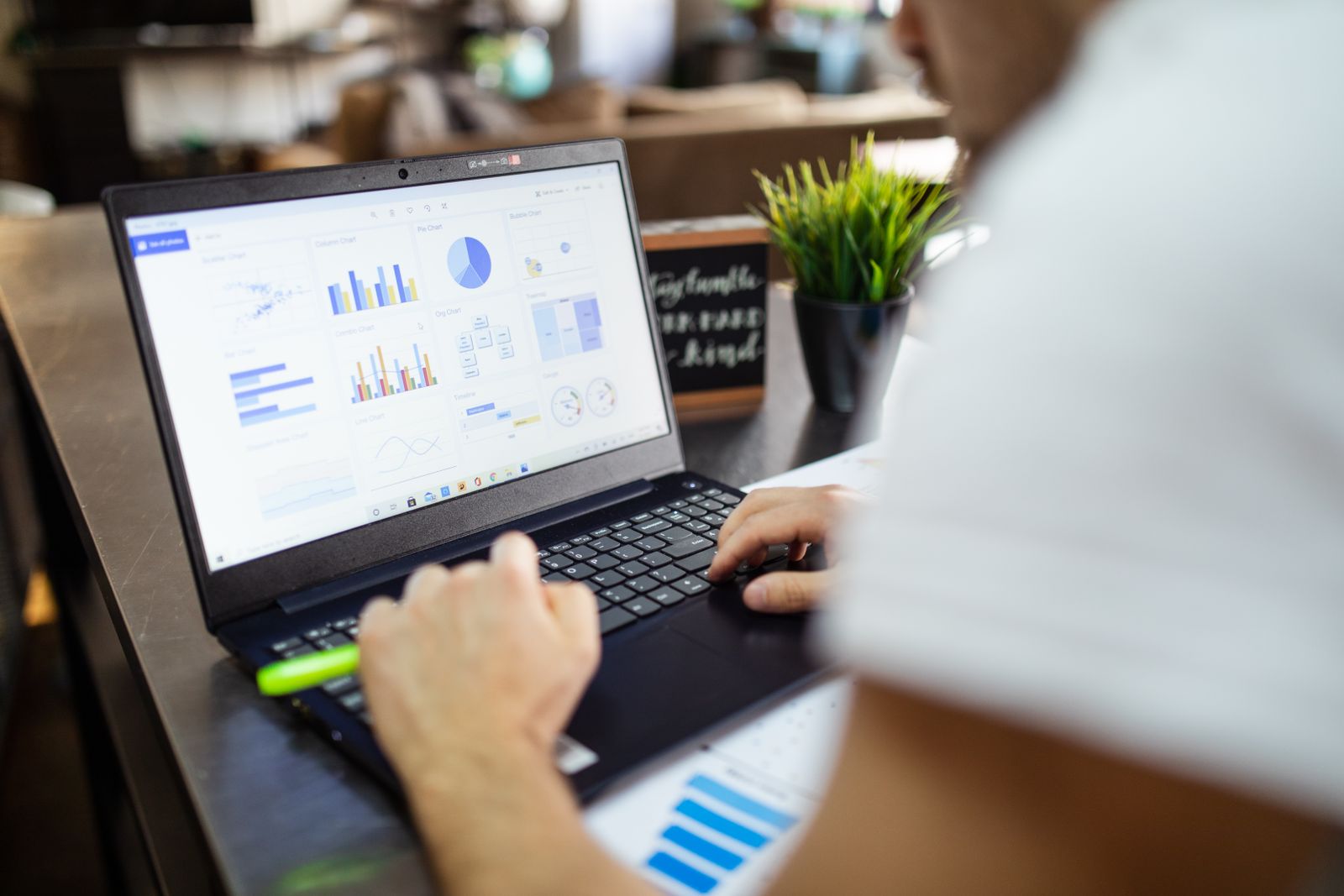 Hands at a laptop showing charts and tables of figures on a desk