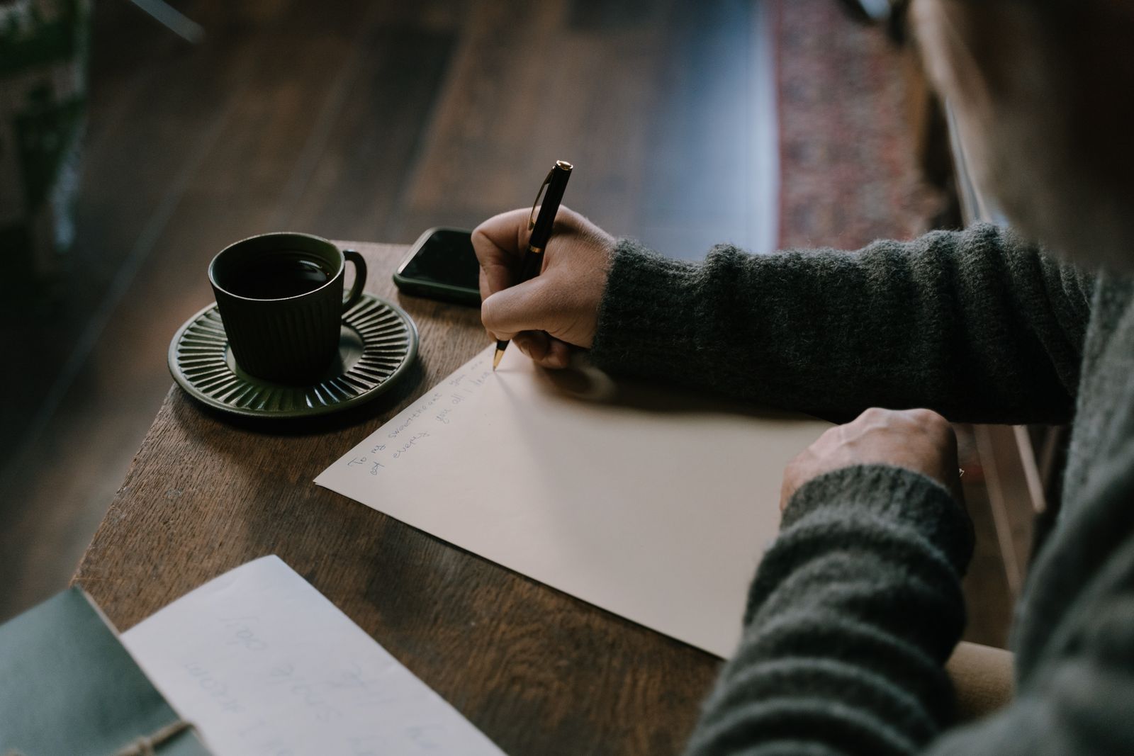 A person writing on paper at a table with a cup of coffee