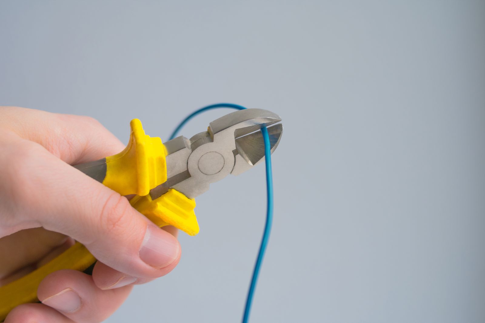 A hand cutting a blue wire with yellow-handled pliers