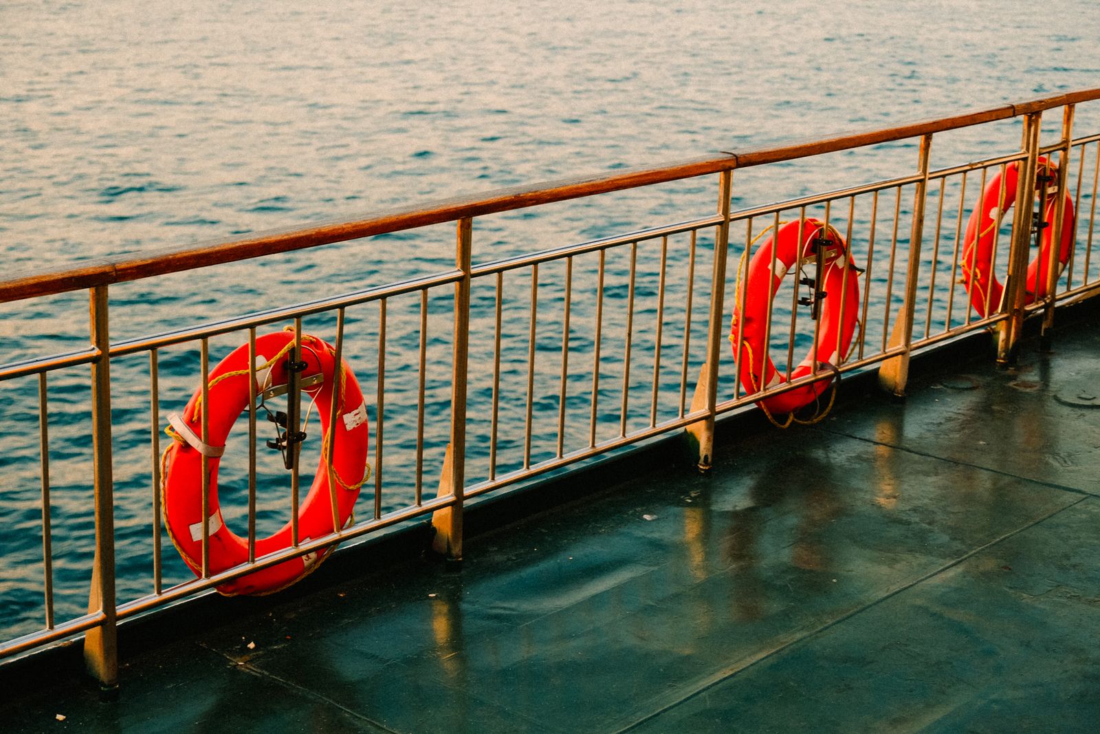 Orange lifebuoys on the railing of a ferry deck above calm sea