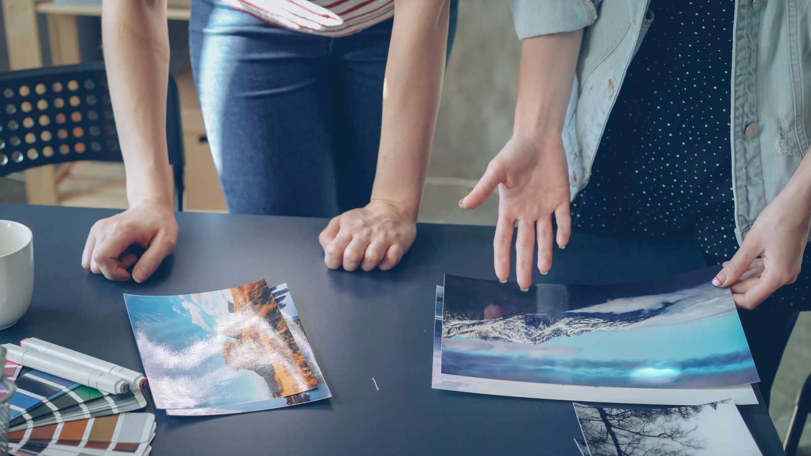 Hands pointing at large printed photographs on a dark table