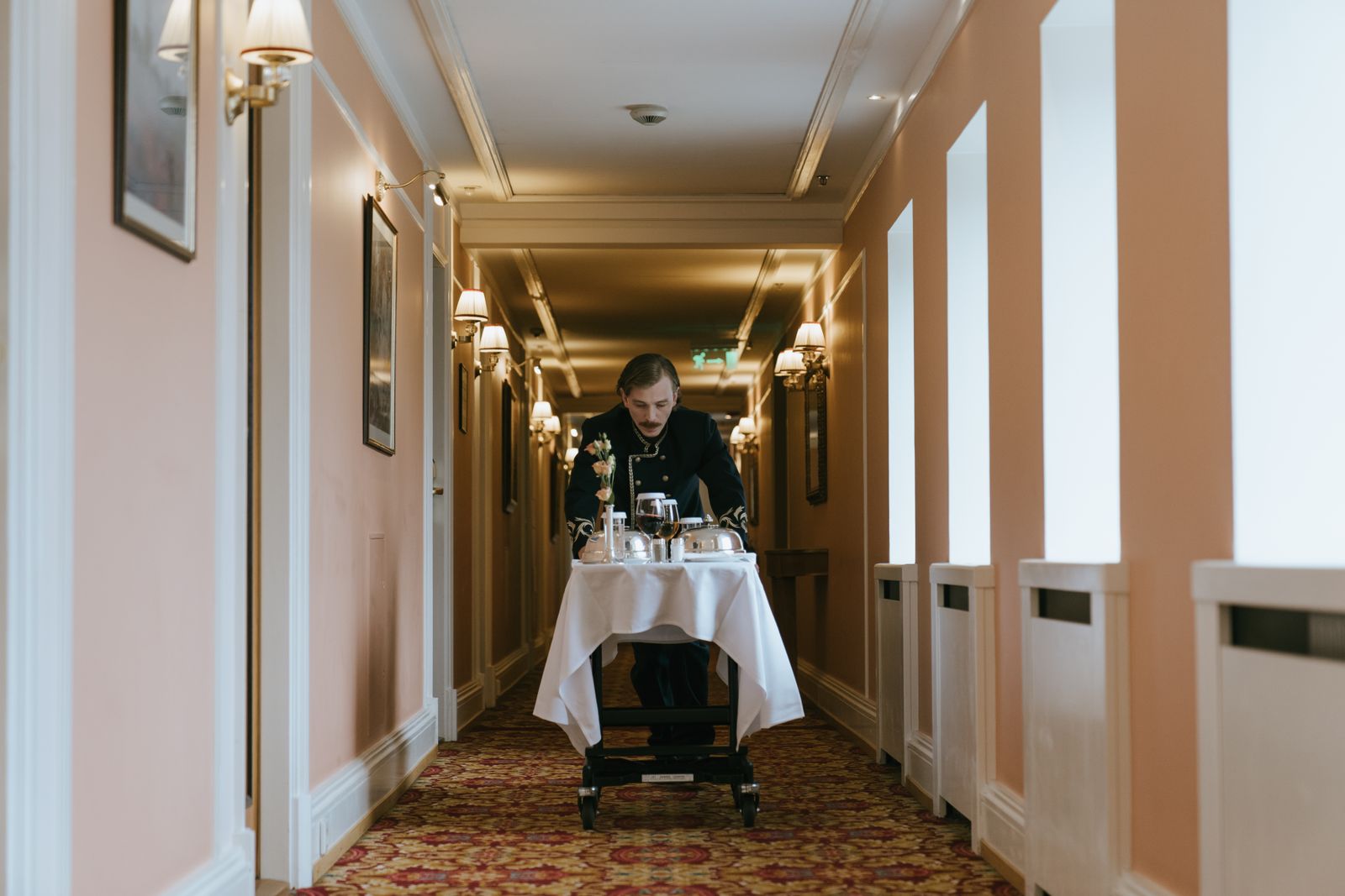 A hotel corridor with a member of staff and a room service trolley