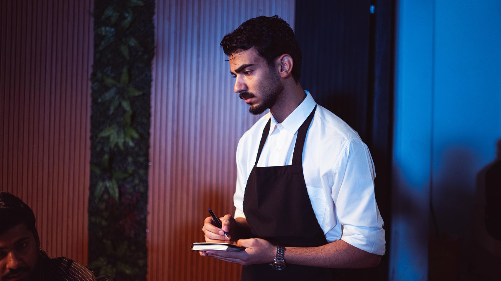 A waiter in an apron writing on a notepad in a restaurant