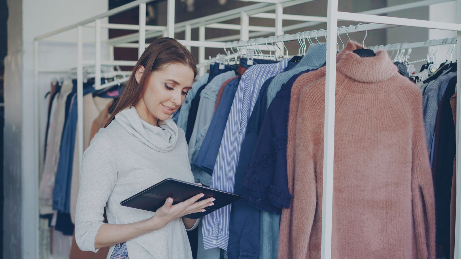 A shop assistant checking a tablet between clothing rails