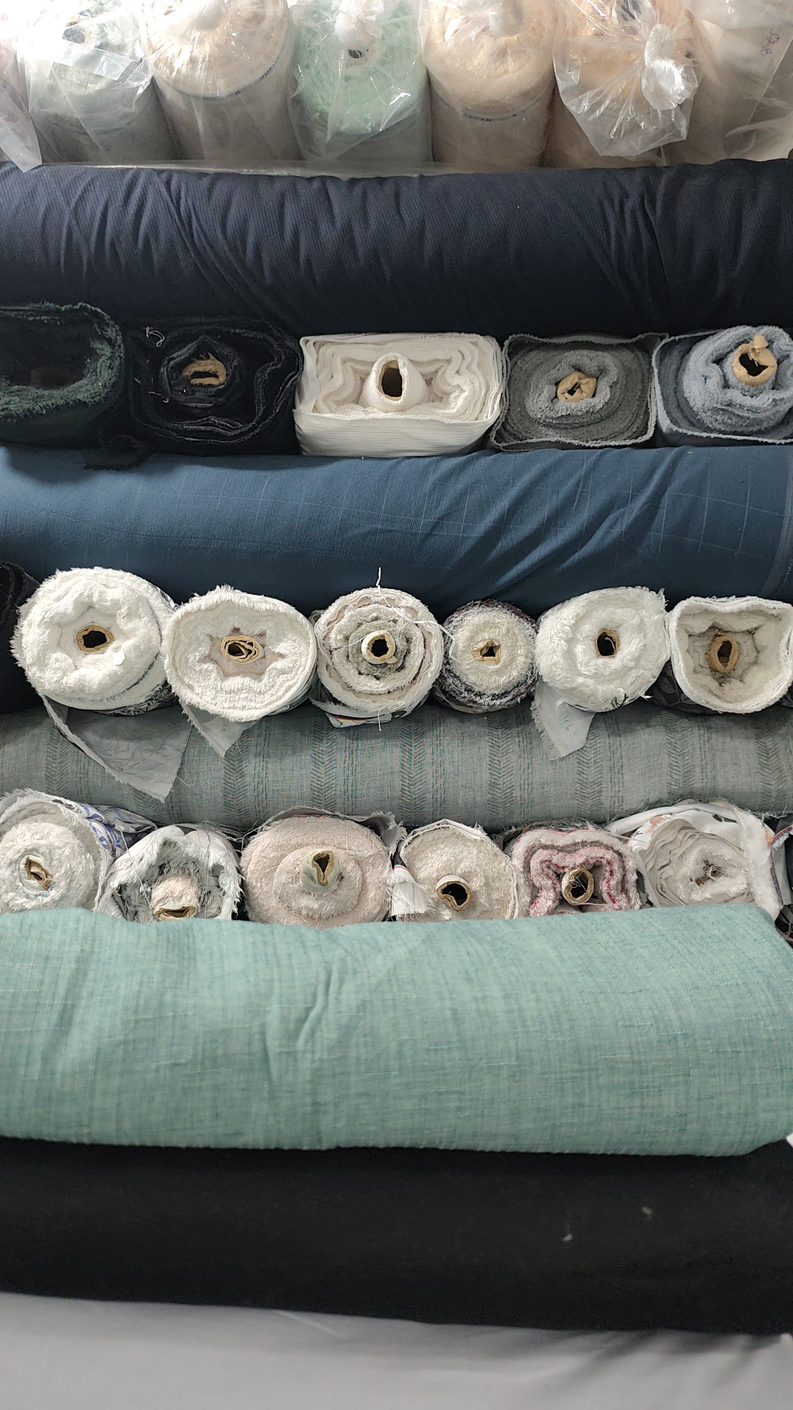 Rolls of undyed and grey wool cloth stacked on shelves