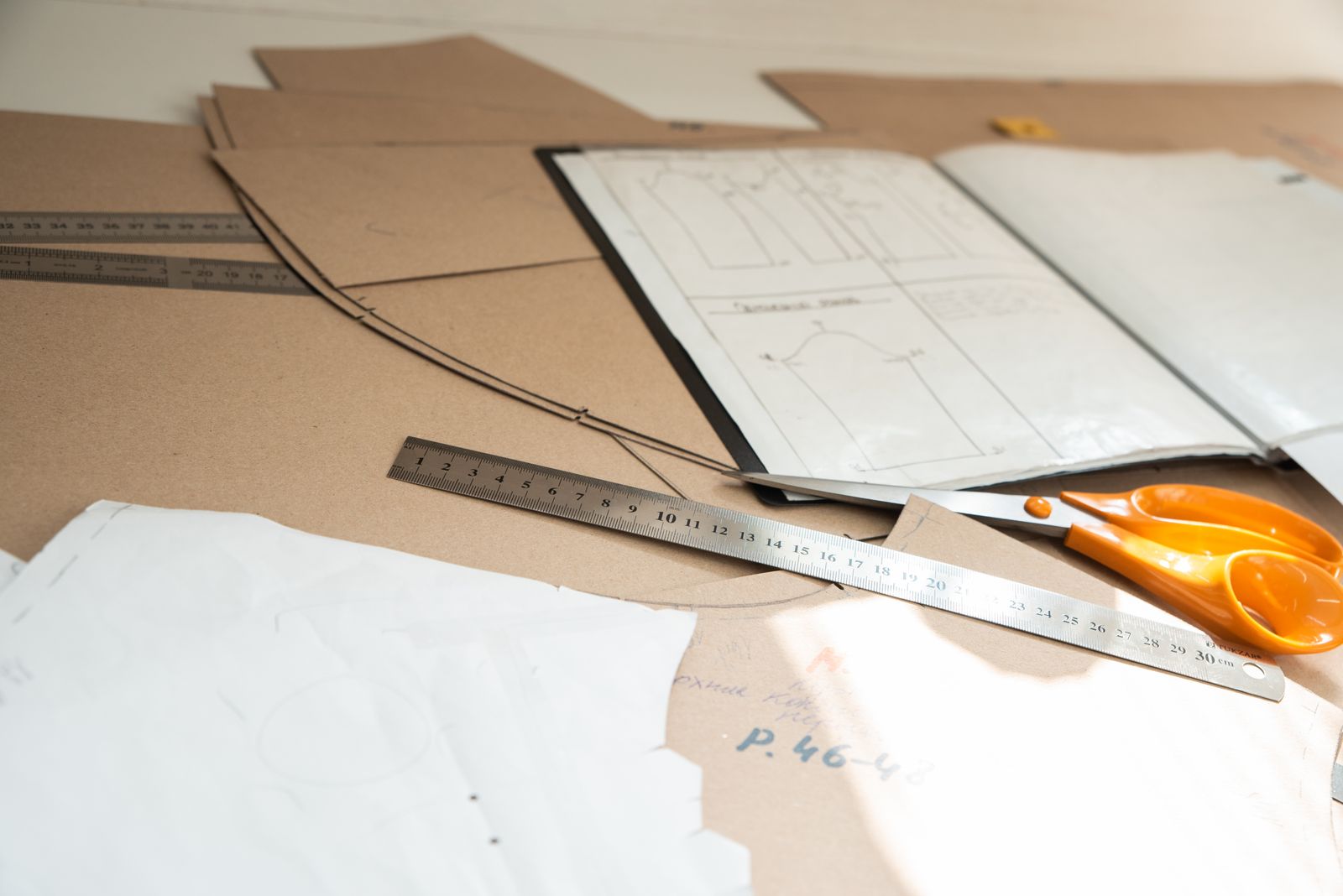 Paper patterns, a metal ruler and orange scissors on a cutting table