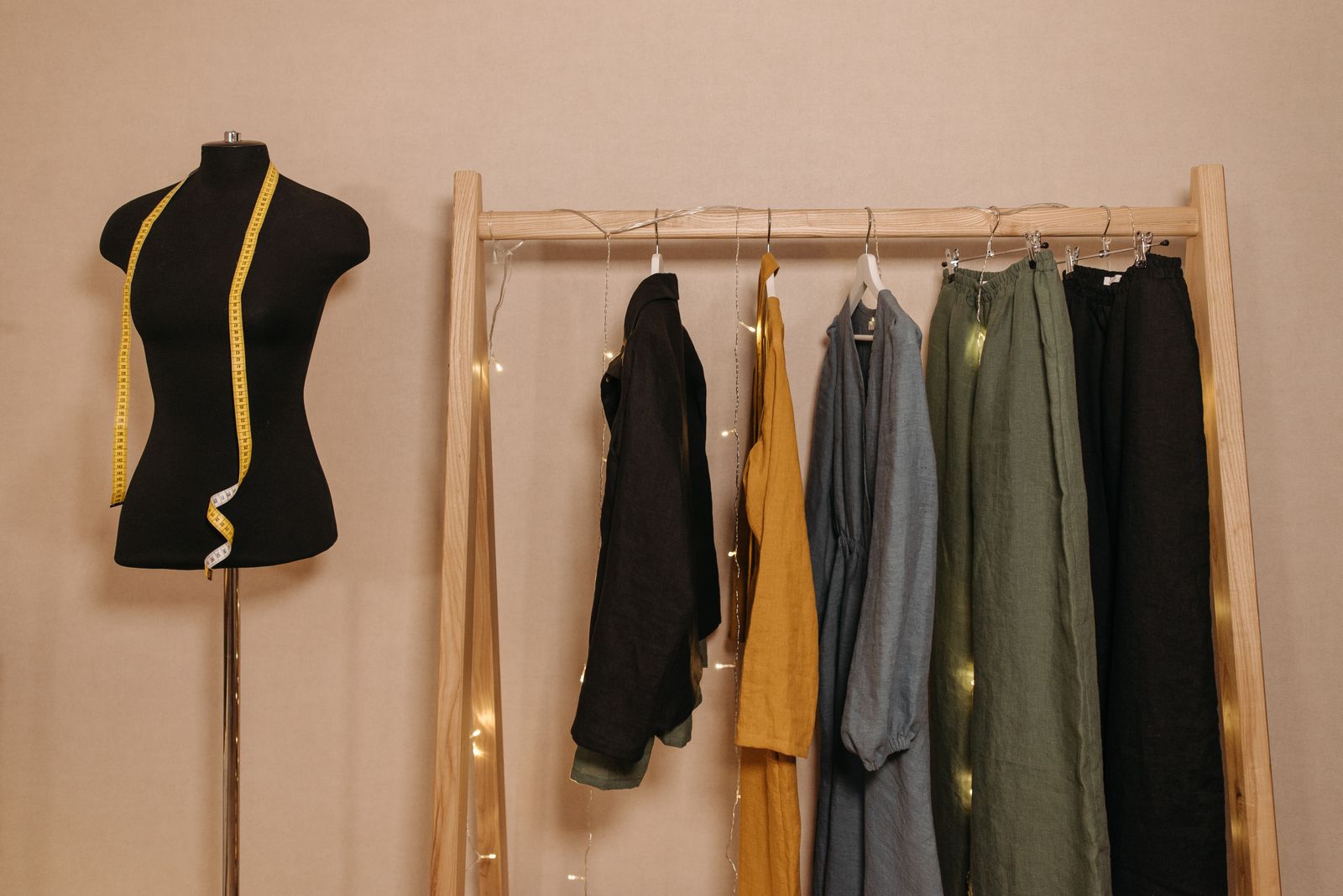 A rail of trousers, jackets and shirts in mustard, olive and black beside a dress form with a tape measure