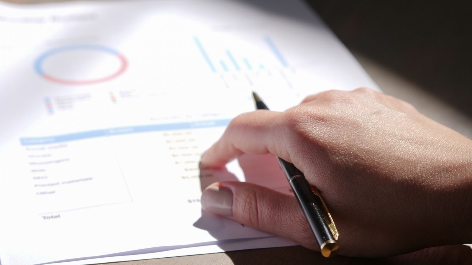 A hand holding a pen over printed charts on paper