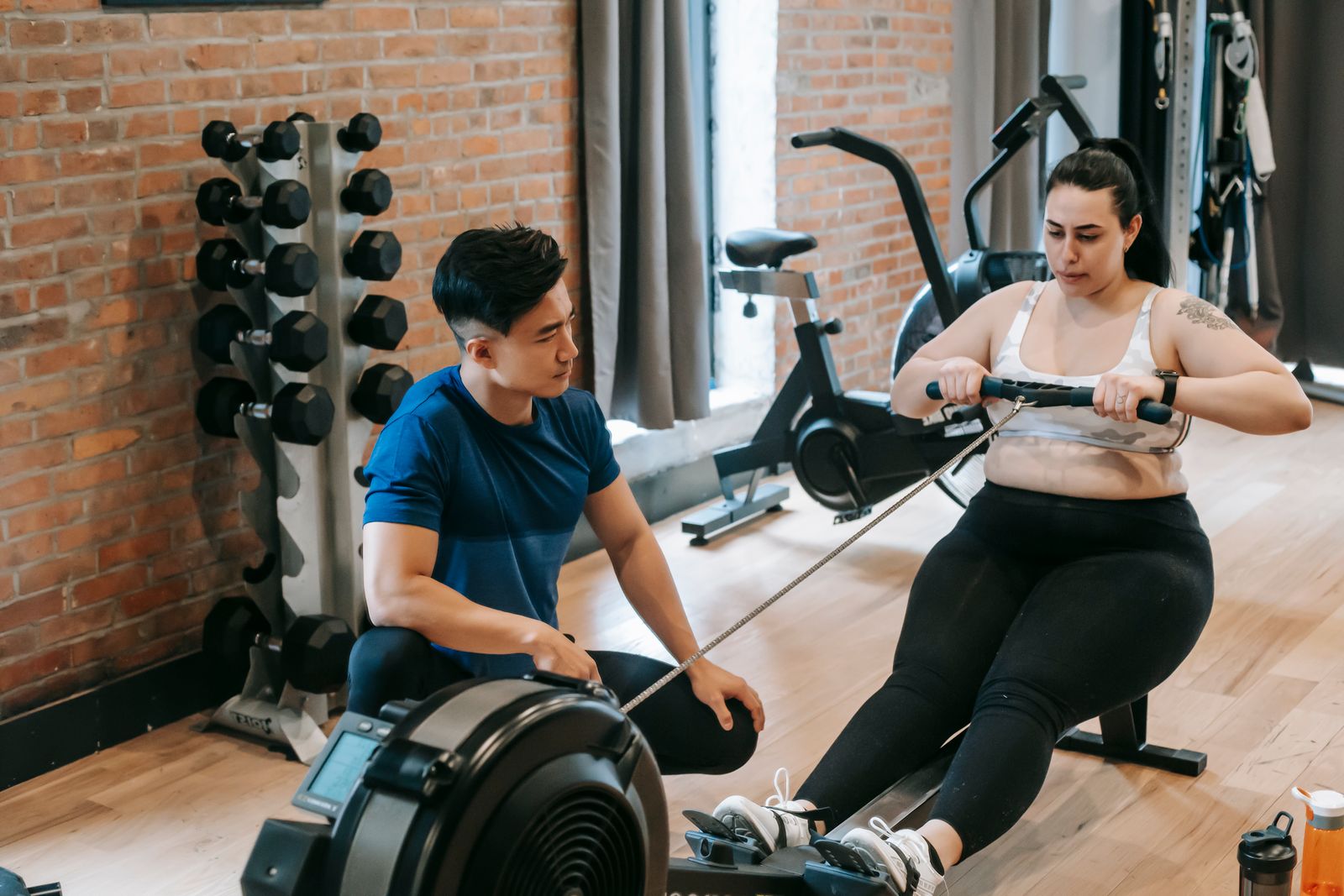 A coach kneels beside a woman working hard on a rowing machine