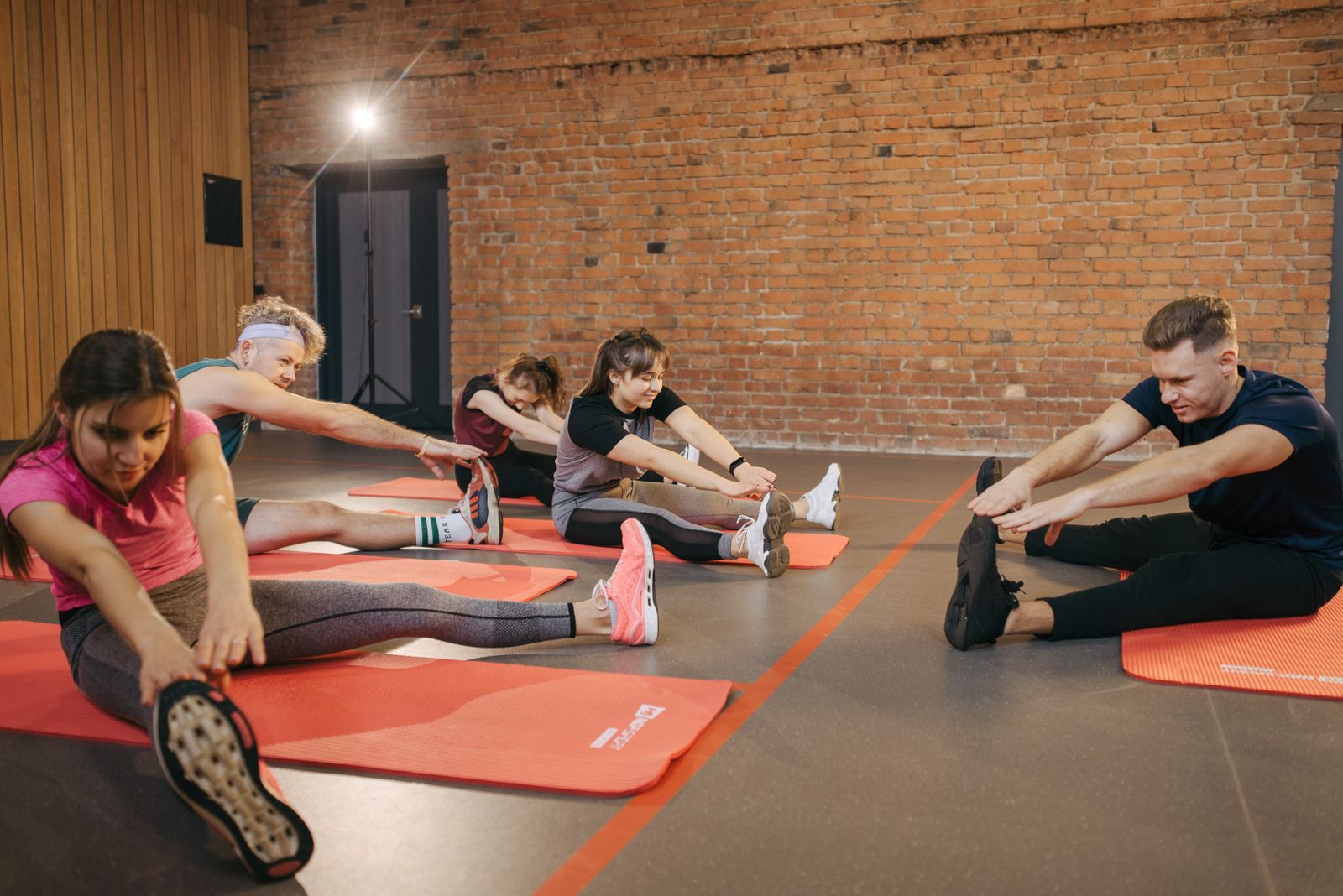 A group stretching on red mats in a brick-walled studio