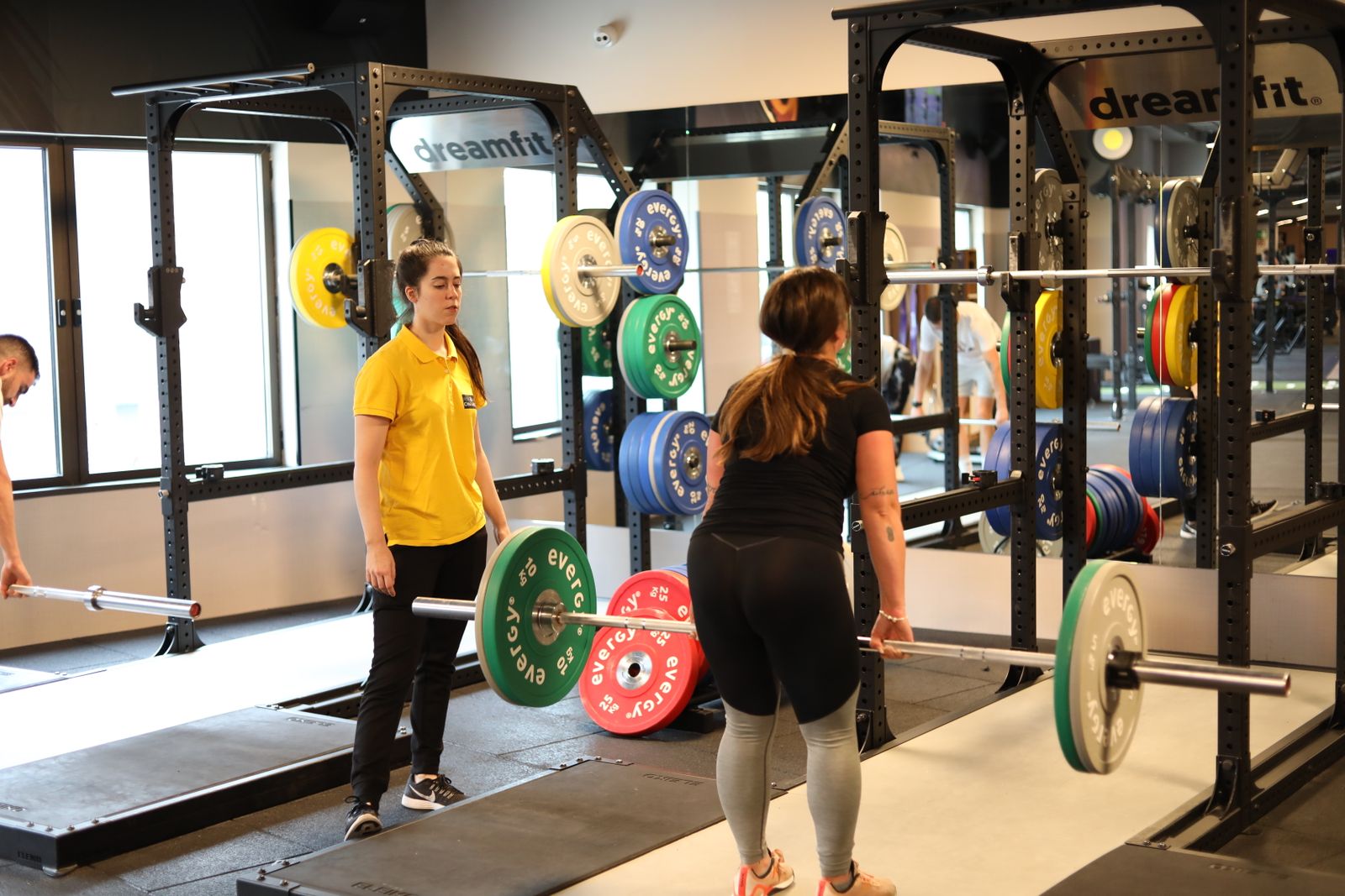 Two women lifting barbells loaded with coloured bumper plates in a bright gym