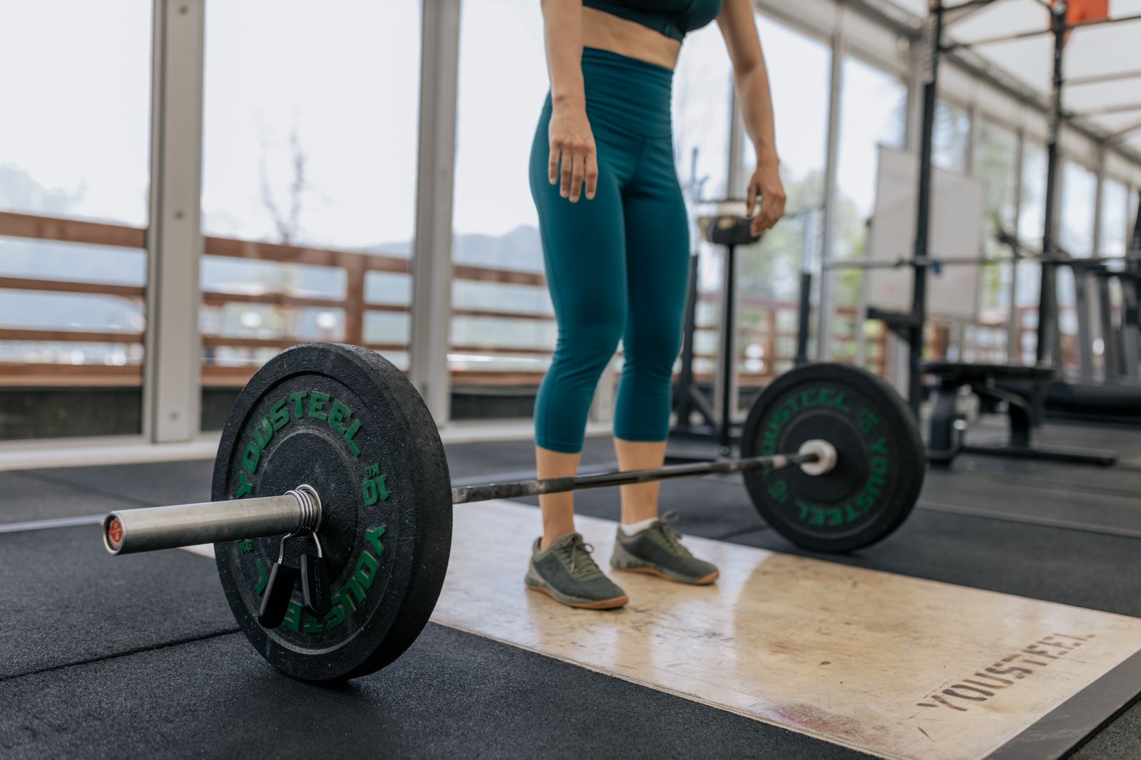 A woman stands over a loaded barbell on a lifting platform before a deadlift