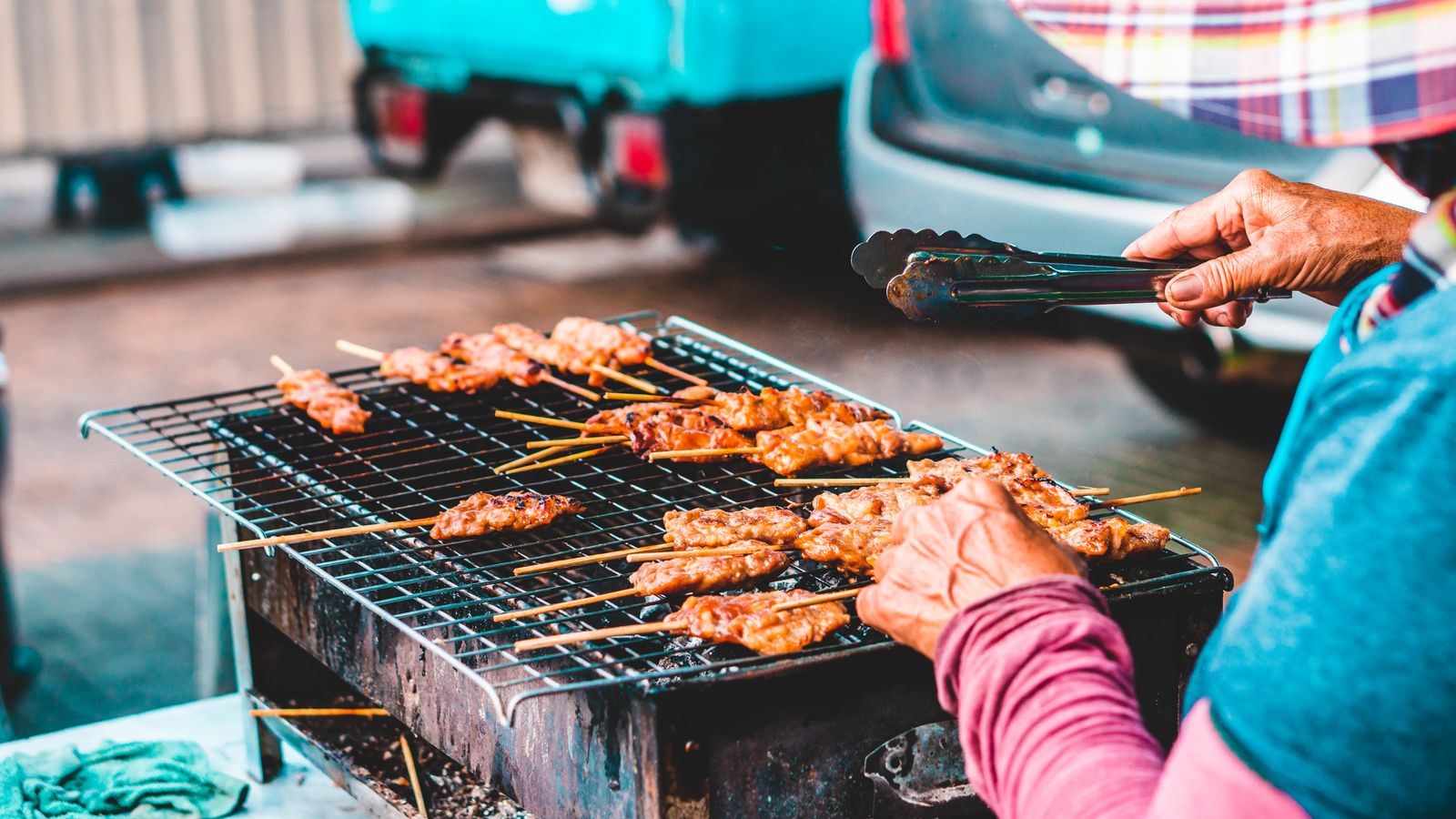 A cook turning chicken skewers on a charcoal grill with tongs