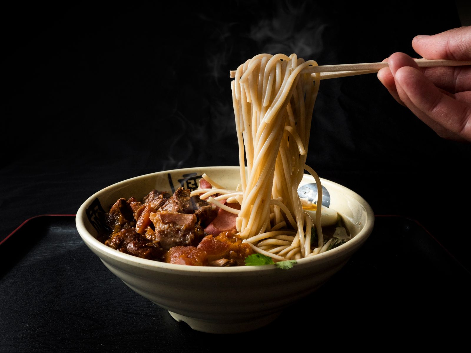 Noodles lifted with chopsticks from a bowl of beef broth, steam rising